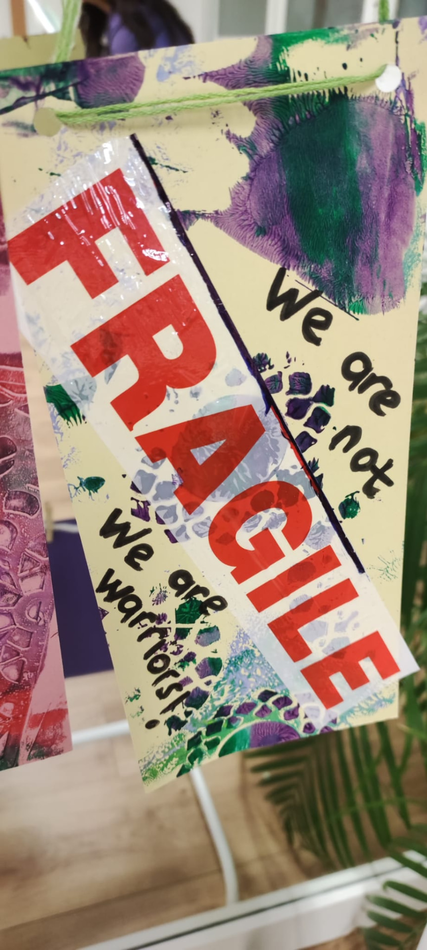 Artwork from the co-created exhibition — a painted banner reading 'Fragile. We are not fragile, we are warriors!'
