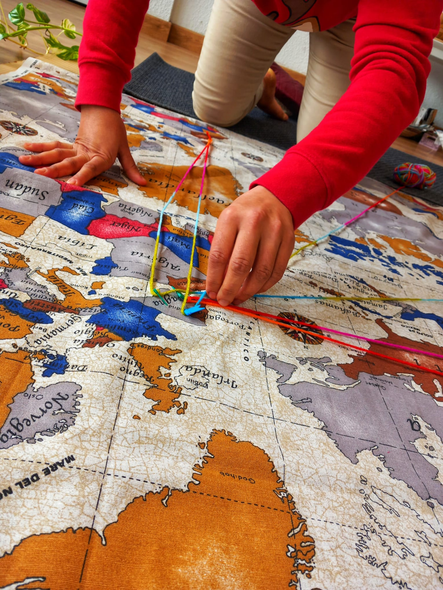 Workshop participant arranging coloured yarn connections across a large fabric world map, from the art therapy workshops